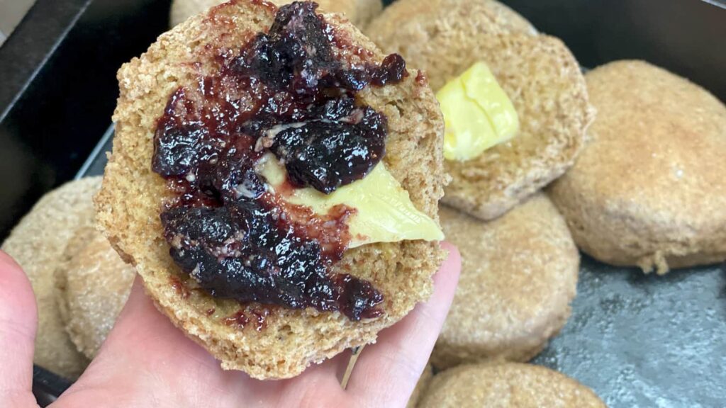Whole wheat biscuit with butter and blackberry preserves in human hand